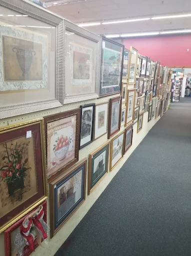 A long wall of framed vintage artwork and antique picture frames inside Timeless Antiques & Flea Mall in Valley Alabama.