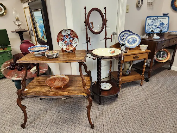 Antique tables displaying decorative plates, dishes, and vintage furniture inside Two Crows Antique Mall in Ranson West Virginia.