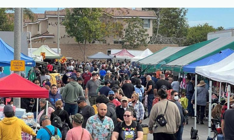 Busy outdoor aisles at Cypress College Swap Meet in Cypress CA showing crowds of shoppers browsing vendor booths with colorful feather flags and pop-up canopy tents lining the parking lot on a sunny weekend morning